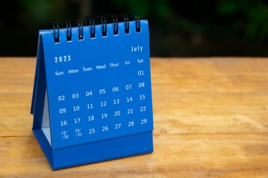 July 2023 blue desk calendar on wooden table background with customizable space for text.