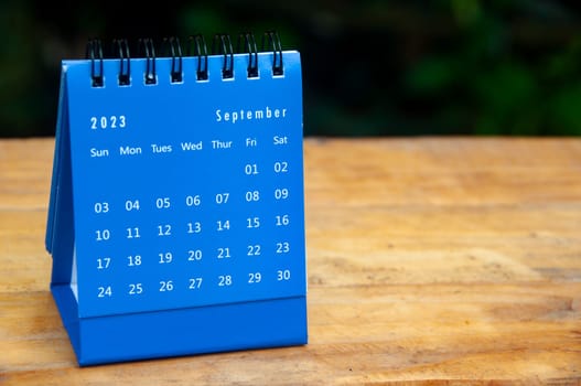 September 2023 blue desk calendar on wooden table background with customizable space for text.