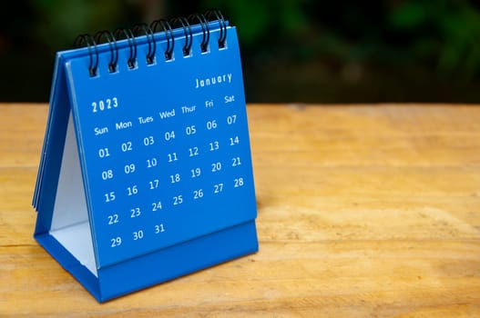 January 2023 blue desk calendar on wooden table background with customizable space for text.