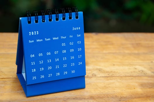 June 2023 blue desk calendar on wooden table background with customizable space for text.