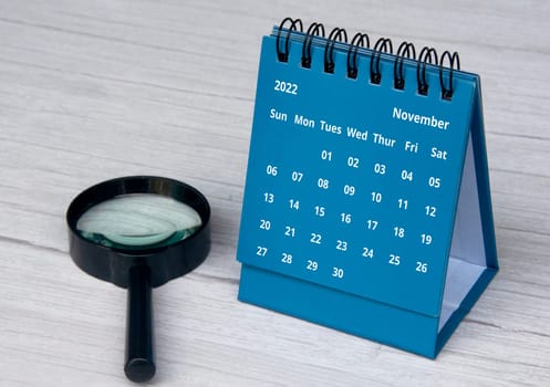 July 2022 blue color desk calendar on wooden desk with copy space and magnifying glass
