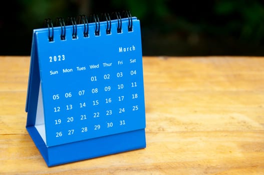 March 2023 blue desk calendar on wooden table background with customizable space for text.