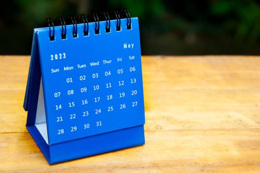 May 2023 blue desk calendar on wooden table background with customizable space for text.
