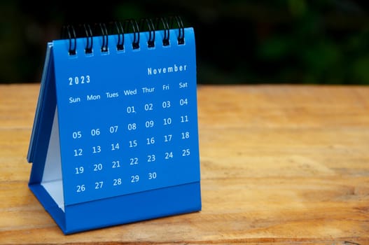November 2023 blue desk calendar on wooden table background with customizable space for text.