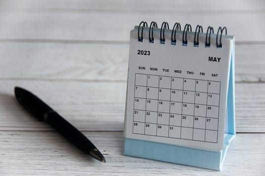 May 2023 white desk calendar with black pen on wooden table. Calendar concept