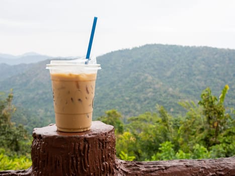 A glass of iced coffee is placed on the fence against a backdrop of mountains and sky.
