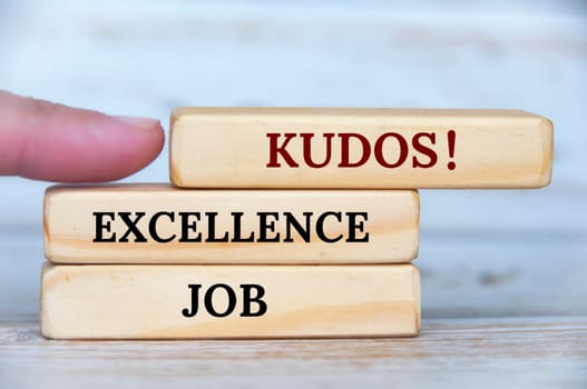 Finger pointing KUDOS text on wooden blocks with wooden cover background. Achievement concept.