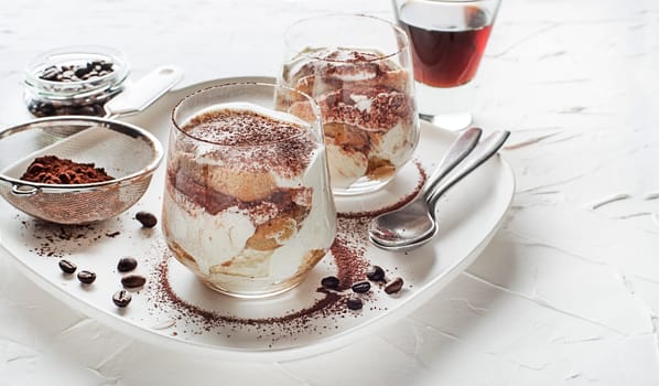 Traditional Italian dessert tiramisu in a glass cup. Homemade tiramisu in glass cup, step by step cooking process. Traditional unbaked Italian dessert on white background. Coffee and mascarpone cream