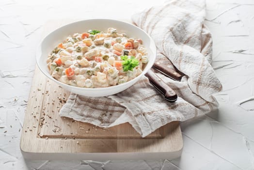 Bowl of russian salad or olivier or french salad with vegetables and egg dressed with mayonnaise on white table