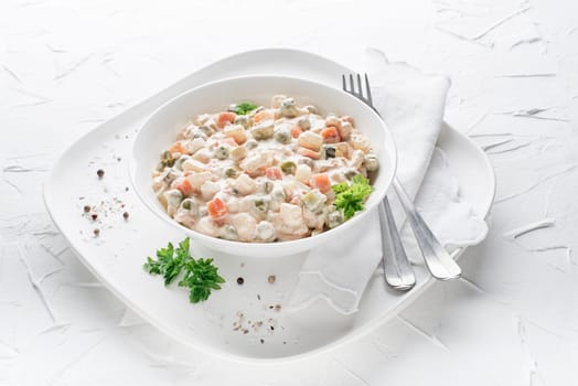 Bowl of russian salad or olivier or french salad with vegetables and egg dressed with mayonnaise on white table