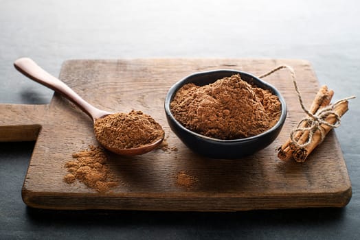 Ground cinnamon in glass cups and cinnamon sticks with powder on grey rustic background