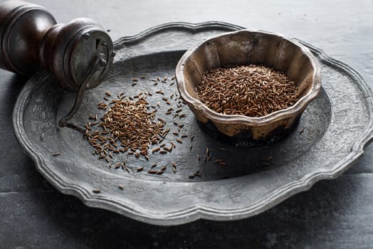 Pile of Cumin seeds and cumin seeds in bowl on grey background close up