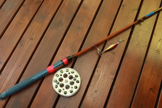 vintage fishing rod with a big reel and a wobbler on a wooden background