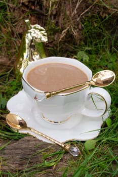 White cup with cold coffee drink on green grass outdoors, vertical image