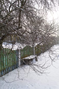 Snow covered wooden bench and fence in the countryside, vertical image