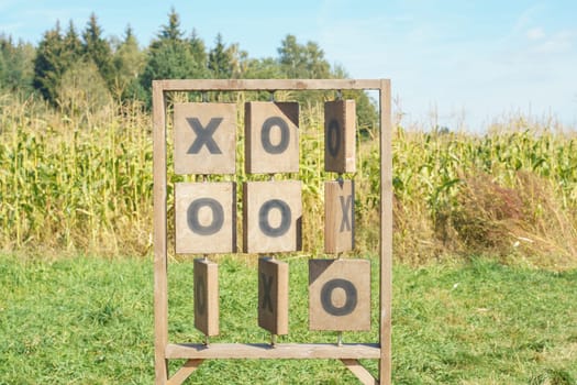 Huge vertical stand of wooden Tic-tac-toe noughts and crosses game installed near cornfields outdoors in field park in summer sunny day. Board games, entertainment, outdoor activity, eco toys, nature.