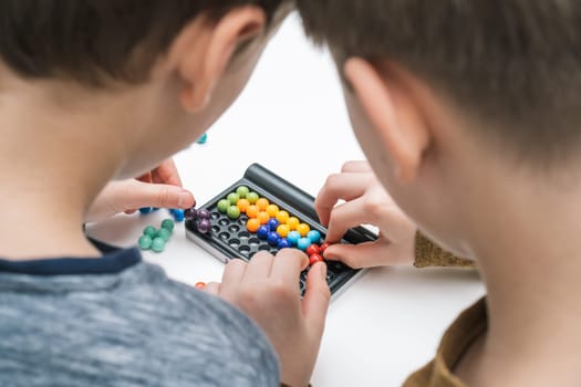 Top view of two boys friends playing colorful 3D puzzle classic pyramid game, putting beads in order on black plastic board. Board games, educational gifts, smart IQ games, intellectual development.