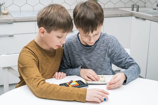 Portrait of two boys friends sitting at table in kitchen at home, reading instruction for playing colorful 3D puzzle classic pyramid game, putting beads in order on black plastic board. Board games.