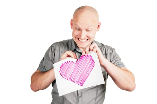 Smiling handsome bald middle-aged man in gray shirt tear pink heart drawn on sheet of paper with pleasure isolated on white background. Valentine's day, hatred, dislike, relations, emotion concept