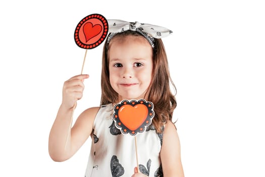 Portrait of cute little girl with long hair holding two paper red hearts of different patterns on sticks and forcing smile isolated on white background. Love, Valentines day, birthday, Mother's day