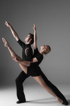 The two young modern ballet dancers in black suits posing over gray studio background