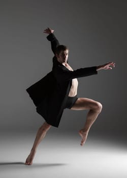 The young attractive modern ballet dancer in black jacket over white background.