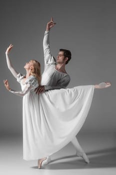 Two young classic ballet dancers practicing. attractive dancing performers  in white suits over gray background