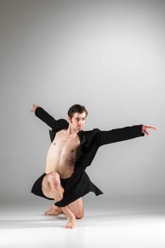 The young attractive modern ballet dancer in black jacket over white background.