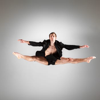 The young attractive modern ballet dancer in black jacket  jumping over gray background