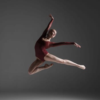 young beautiful modern style dancer jumping on a studio gray background