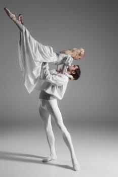 Two young classic ballet dancers practicing. attractive dancing performers  in white suits over gray background
