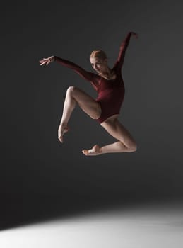 young beautiful modern style dancer jumping on a studio gray background