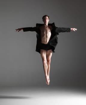 The young attractive modern ballet dancer in black jacket  jumping over gray background