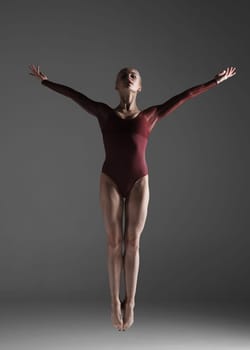 young beautiful modern style dancer jumping on a studio gray background