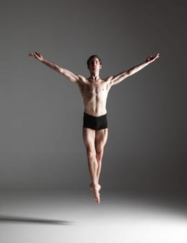 The young attractive modern ballet dancer jumping over gray background