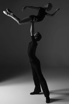 The two young modern ballet dancers in black suits posing over gray studio background