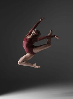 young beautiful modern style dancer jumping on a studio gray background