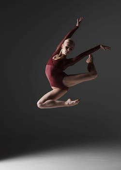 young beautiful modern style dancer jumping on a studio gray background