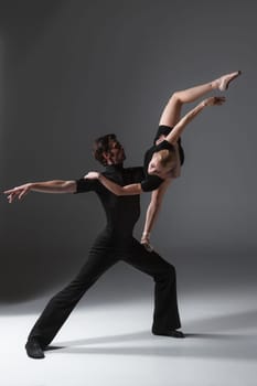 The two young modern ballet dancers in black suits posing over gray studio background
