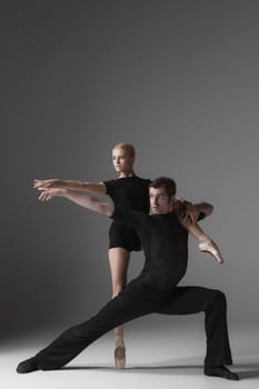 The two young modern ballet dancers in black suits posing over gray studio background