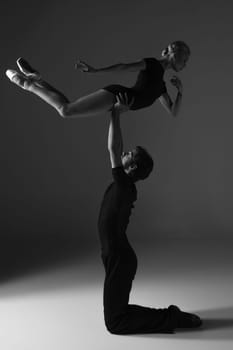 The two young modern ballet dancers in black suits posing over gray studio background