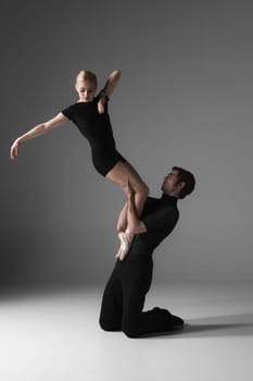 The two young modern ballet dancers in black suits posing over gray studio background