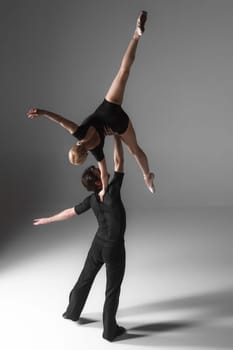 The two young modern ballet dancers in black suits posing over gray studio background