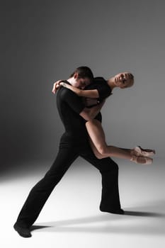 The two young modern ballet dancers in black suits posing over gray studio background