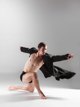 The young attractive modern ballet dancer in black jacket over white background.