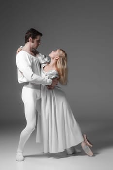 Two young classic ballet dancers practicing. attractive dancing performers  in white suits over gray background