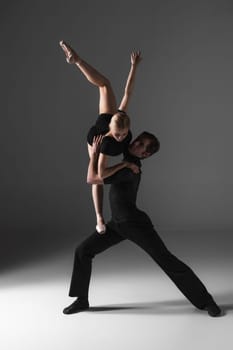 The two young modern ballet dancers in black suits posing over gray studio background