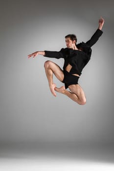 The young attractive modern ballet dancer in black jacket  jumping over gray background