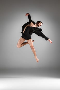 The young attractive modern ballet dancer in black jacket  jumping over gray background