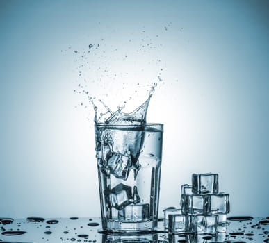 ice cubes falling into a glass of water and ice cubes, lying next, on blue background
